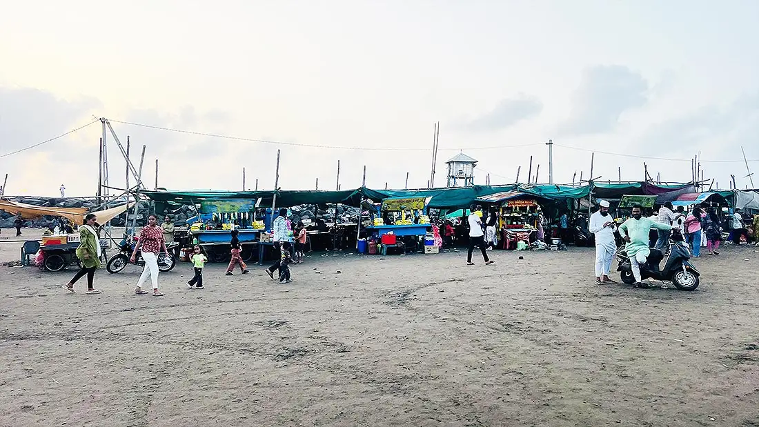 Row of food stalls at Dumas Beach Surat with visitors walking on sandy beach