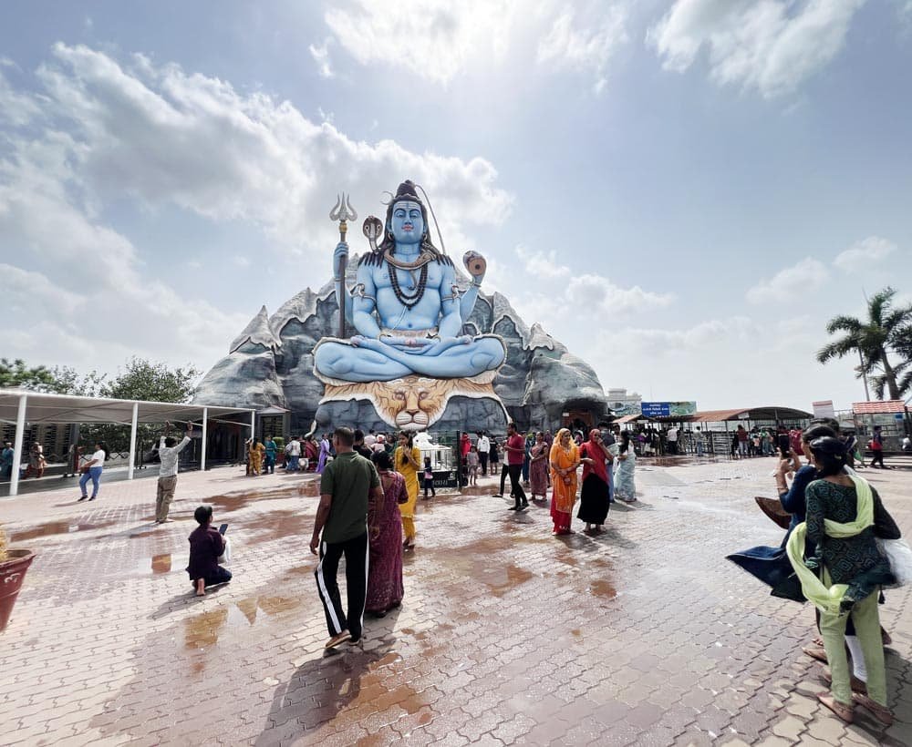 Huge blue statue of Lord Shiva seated on a tiger with devotees gathered at Galteshwar Mahadev Temple